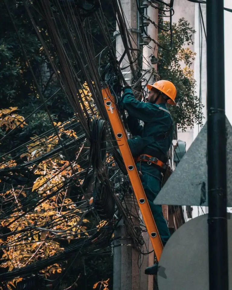 Electrician in a hard hat on a fiberglass ladder working an overhead cable bundle